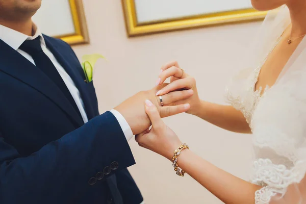 Les jeunes mariés échangent des bagues, le marié met la bague sur la main des mariées dans le bureau d'enregistrement du mariage. — Photo