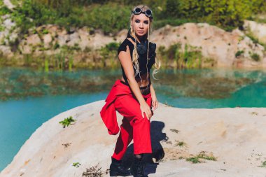 Steampunk takım elbiseli bir kadın kollarını kavuşturarak meydan okuyan bir tavır takındı. Kirli bir gölün arka planında solunum cihazı var.