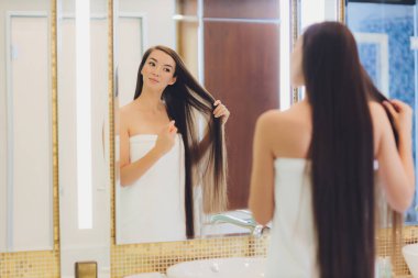 Genç bir kadın saçına yağ sürüyor, kapalı alanda..