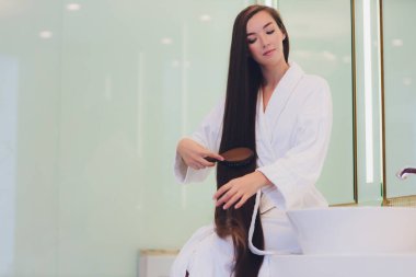 Genç hamile bir kadın banyoda uzun saçlarını tarıyor..