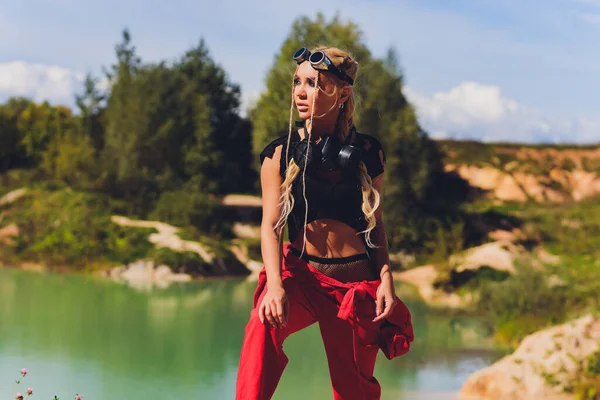 Mulher vestida com um terno steampunk em uma atitude desafiadora com os braços cruzados. respirador no rosto, contra o fundo de um lago sujo — Fotografia de Stock