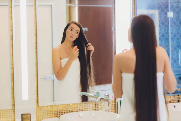 Junge Frau trägt Öl auf ihr Haar auf, drinnen. — Stockfoto