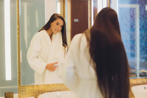 Een jonge vrouw staat in een badkamer en droogt haar haar met een handdoek. Ze kijkt naar de spiegel. Horizontaal ingelijste opname. — Stockfoto