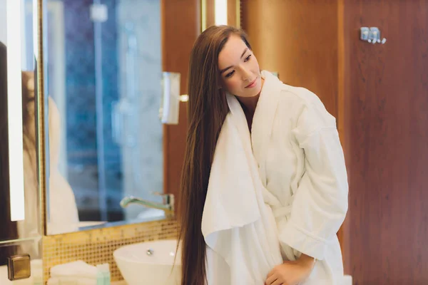 Een jonge vrouw staat in een badkamer en droogt haar haar met een handdoek. Ze kijkt naar de spiegel. Horizontaal ingelijste opname. — Stockfoto