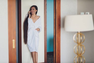 İnsanlar, güzellik, yaşam tarzı, teknoloji ve rahatlama konsepti - beyaz banyo bornozlu, akıllı telefonlu ve kaplıcada konuşan güzel bir kadın.