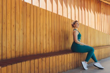 Güzel genç fitness eğitmeni, sokakta tahta bir verandada dizüstü bilgisayar kullanarak video dersleri veriyor..