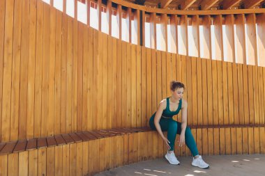 Güzel genç fitness eğitmeni, sokakta tahta bir verandada dizüstü bilgisayar kullanarak video dersleri veriyor..