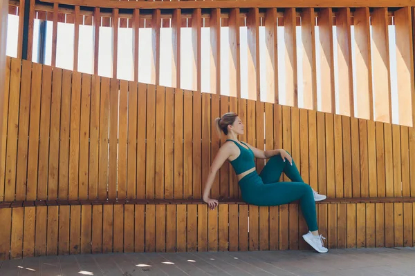 Belle jeune instructeur de fitness donne des leçons sur vidéo à l'aide d'un ordinateur portable sur une véranda en bois dans la rue. — Photo