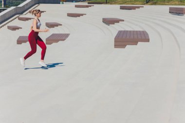 Koşan kadın. Koşucu gün doğumunda koşuyor. Şehrin dışında bir rıhtımda kadın fitness modeli eğitimi. Spor yaşam tarzı.