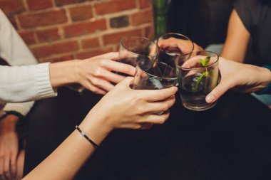 Bokeh arkaplanının önünde kadeh tokuşturup şampanya içen bir grup insanı yakından çek. Yaşlı insanların elleri.