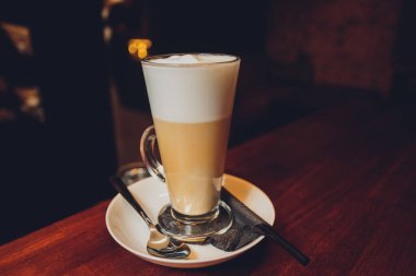 Sıcak latte macchiato kahve, üstünde karamel sanatları ve uzun ve berrak bardakla servis ediliyor..
