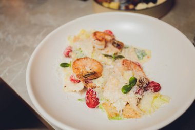 Kare beyaz tabakta, karidesli Sezar salatası. İştah açıcı deniz ürünleri. Izgara parmesan. Yaklaş, seçici odaklanma.