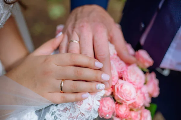 カラフルな結婚式の花束を保持する新婚夫婦の手のクローズアップビュー。新郎新婦の結婚指輪を着ている。屋外の背景。結婚式の日のコンセプト. — ストック写真