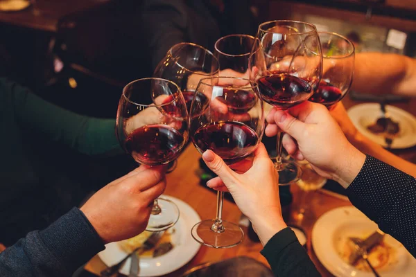 Közelkép emberek csoportjáról, akik poharakat csörömpölnek borral vagy pezsgővel bokeh háttér előtt. idős emberek kezei. — Stock Fotó