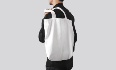 Adam çanta tuval kumaş mockup boş şablon gri arka plan üzerinde izole için tutuyor. 