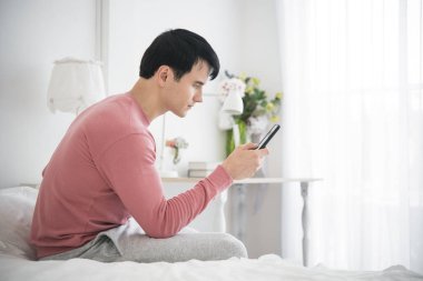 Evde yatak odasında ileti için bir cep telefonu kullanan adam.