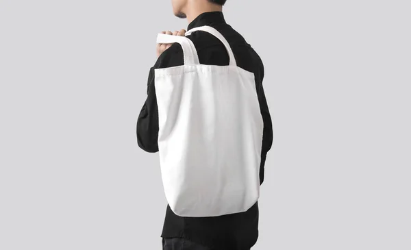 Adam çanta tuval kumaş mockup boş şablon gri arka plan üzerinde izole için tutuyor. 