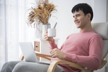 Kahve içme ve sabah zamanında bilgisayar kullanarak bir genç adam. kavram uyan