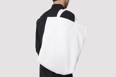 Adam çanta tuval kumaş mockup boş şablon gri arka plan üzerinde izole için tutuyor. 