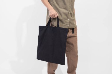 Holding siyah çanta tuval kumaş mockup boş şablon gri arka plan üzerinde izole için adamdır. 