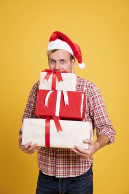 Yakışıklı adam sarı arka planda bir sürü hediye kutusu tutan Noel Baba şapkası takıyor. Noel ve mutlu yıllar konsepti.