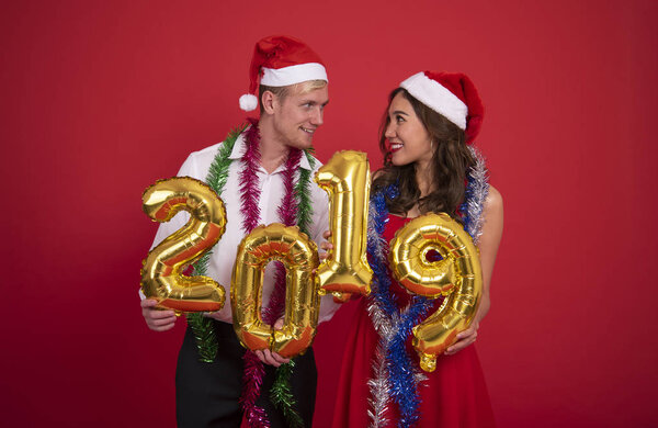 Portrait young couple carrying gold colored numbers 2019 on red background. celebration christmas and happy new year concept. 