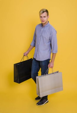 Sarı arka plan üzerinde alışveriş kağıt torba tutarak portre yakışıklı adam.