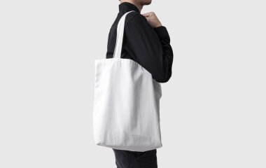 Adam çanta tuval kumaş mockup boş şablon gri arka plan üzerinde izole için tutuyor. 