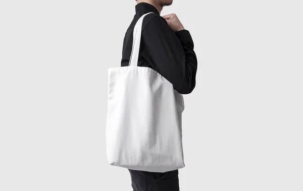 Adam çanta tuval kumaş mockup boş şablon gri arka plan üzerinde izole için tutuyor. 