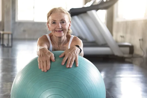 senior at yoga gym posing leaning on her ball smiling and happy. elderly healthy lifestyle.
