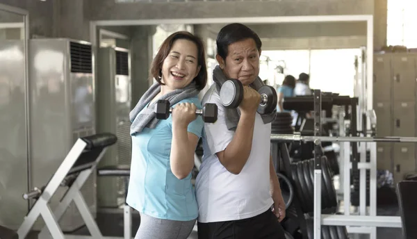 Asian senior man and woman exercise lifting dumbbell in fitness gym. elderly healthy lifestyle.