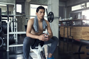 Genç Asyalı sportif adam fitness jimnastik salonu iş sonra havlu ile oturmuş yorgun.