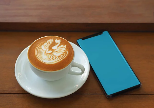 Пустой экран мобильного телефона с кофе капучино на деревянном столе — стоковое фото