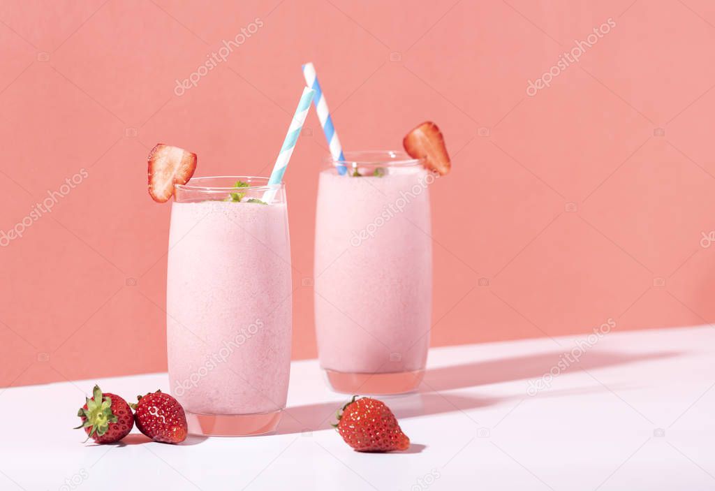 Strawberry smoothie in glass with straw and scattered berries 