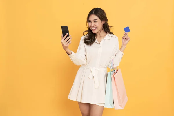 Азіатські жінки shopper за допомогою мобільного телефону та кредитну картку для здійснення платежів. Чорна п'ятниця і покупки онлайн концепція ізольовані на жовтому фоні. — стокове фото