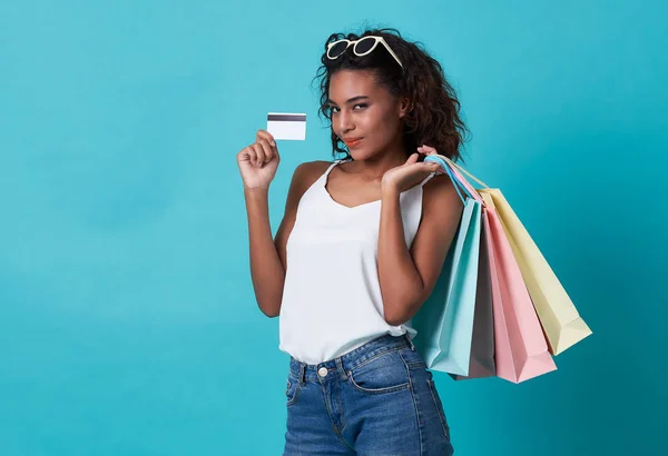 Porträtt av en ung afrikansk kvinna som visar kreditkort och shoppingväska isolerad över Blå bakgrund. — Stockfoto