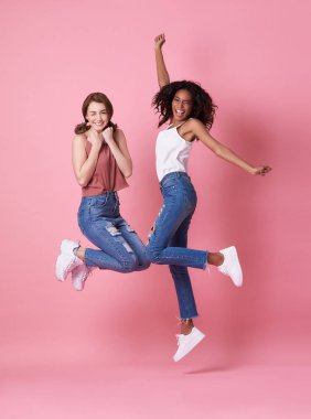 İki neşeli genç kadın portre atlama ve pembe arka plan üzerinde kutluyor.