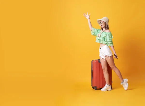 Veselá mladá žena oblečená v letních šatech s kufříkem a pozdravila v prostoru pro kopírování, izolovaná přes žluté pozadí. — Stock fotografie