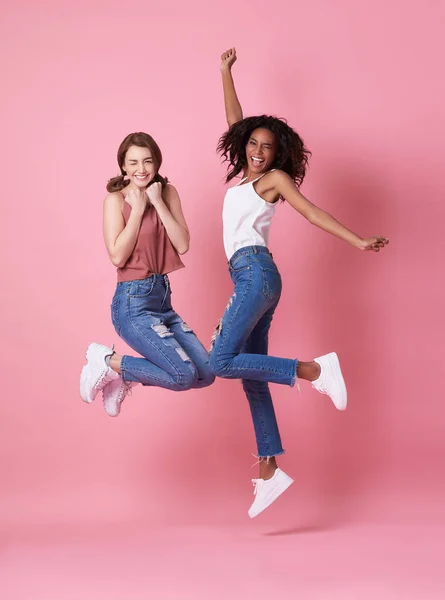 Retrato de dos jóvenes alegres saltando y celebrando sobre fondo rosa . — Foto de Stock