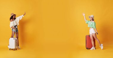 Neşeli arkadaşlar tebrik ve bir bavul ile ayakta yazlık giysiler giymiş toplantı ve sarı arka plan üzerinde izole kopya alanda merhaba demek.