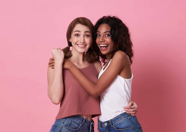 Retrato de dos mujeres jóvenes felices y abrazadas juntas sobre fondo rosa . — Foto de Stock
