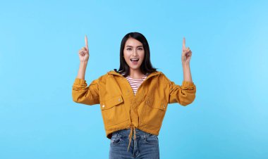 Gülümseyen mutlu Asyalı kadın parmağını açık mavi afiş üzerinde izole edilmiş fotokopi aletiyle işaret ediyor..