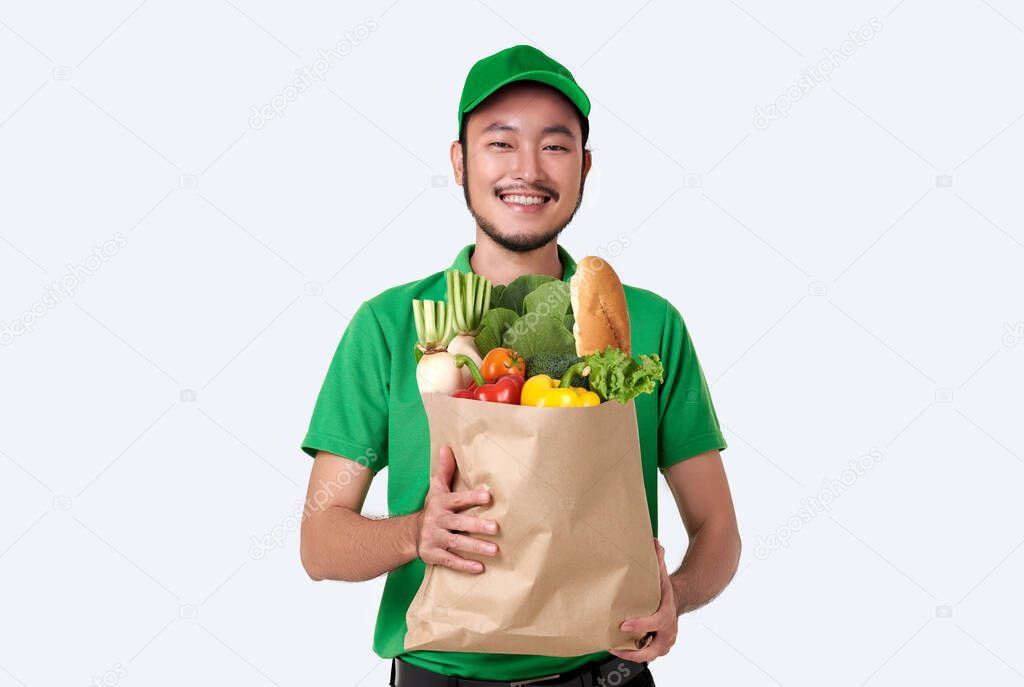 Asian delivery man wearing in green uniform holding fresh food paper bag isolated over white background. 