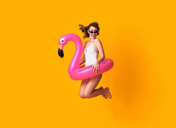 Счастливая Молодая Женщина Прыгает Желтом Фоне Одетая Купальники Держа Фламинго — стоковое фото
