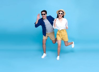 Mutlu enerjik Asyalı çift tatillerde seyahat etmek için mavi arka planda tek başına koşuyor..