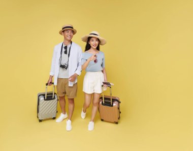 Yaz tatili kıyafeti ve bavul giymiş mutlu Asyalı çift sarı arka planda izole edilmiş tatillerini dört gözle bekliyor..