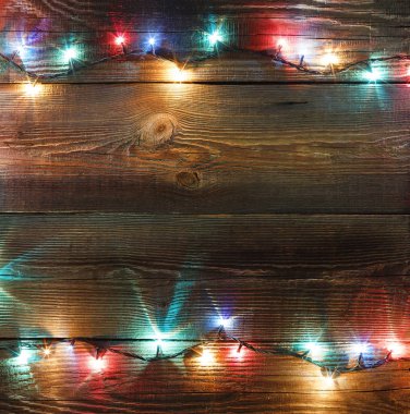 Yeni yıl çerçeve. Noel arka plan. Noel çelenk ile renkli ışıkları ve lambaları bir ahşap zemin üzerinde. Metin için özgür yer. Kopya spase