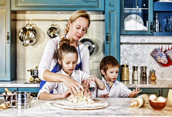 mother\'s day. happy young beautiful mother cooking dough for baking with her children at home in the kitchen. having fun