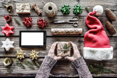El yapımı yılbaşı veya Christmas.Human elleri dolu yeni yıl hediyesi, aksesuarları, tablet bilgisayar ile boş perde ahşap bir masa ve kabarık çam dalları üzerinde yan yana bulunmaktadır. üstten görünüm