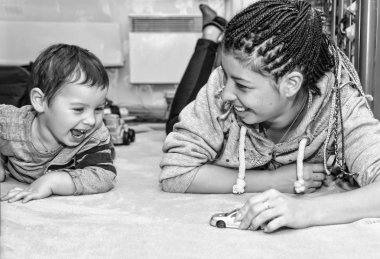 Siyah ve beyaz fotoğraf. Evde oturma odasında oyuncaklarla oynarken mutlu küçük kız. Mutlu aile evde birlikte vakit.